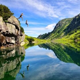 Two travellers enjoy their adventure by jumping off a cliff into water