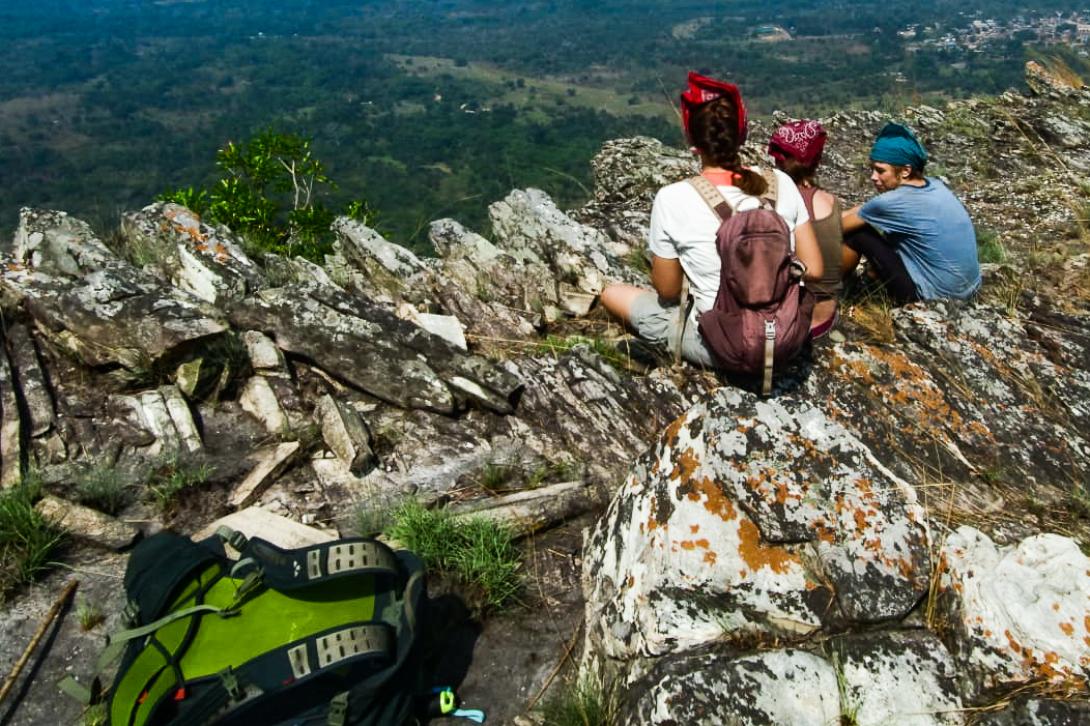 Three backpackers sit on a mountain top in Ghana