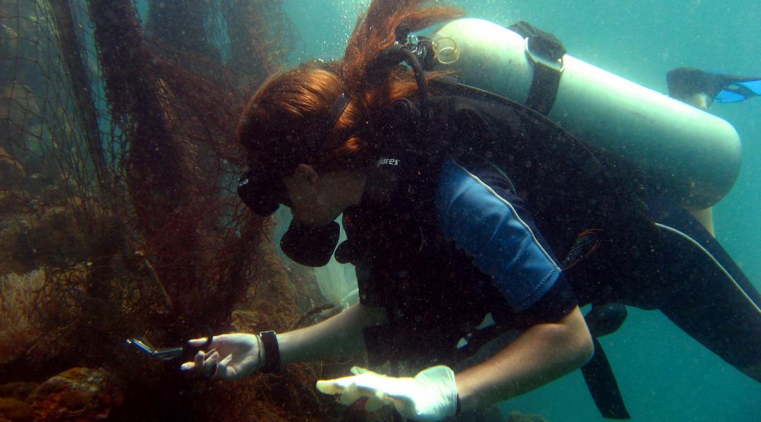 Female volunteer uses scissors to cut a net tangled in the coral reef in Thailand