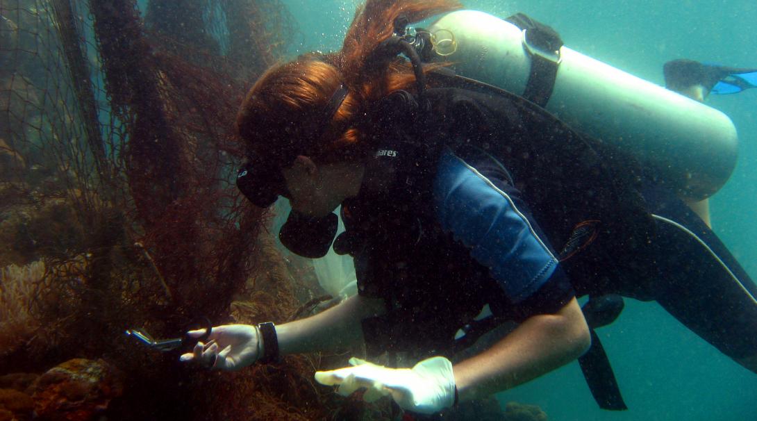 Female volunteer uses scissors to cut a net tangled in the coral reef in Thailand