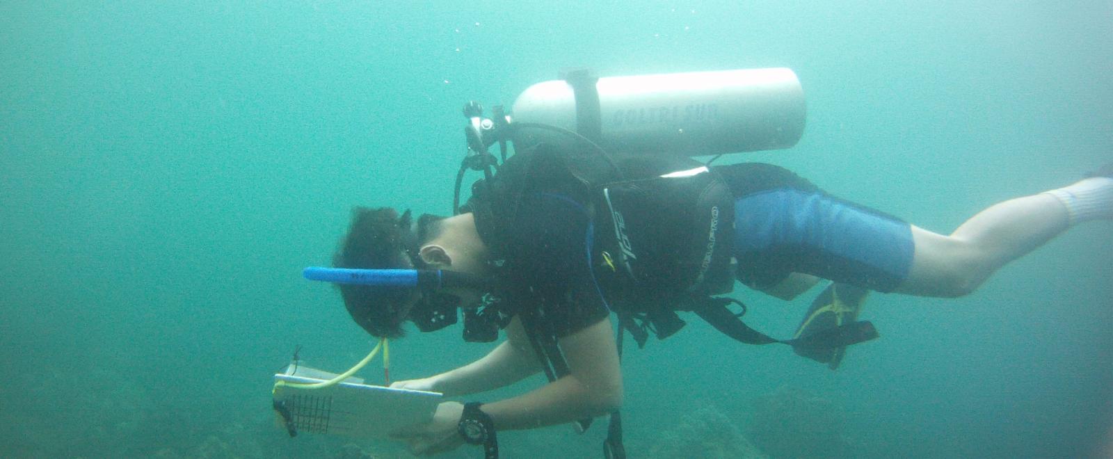 A Projects Abroad volunteer taking his divemaster course and checking notes underwater