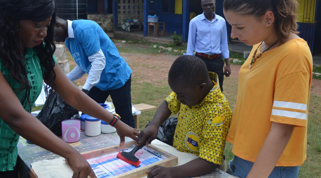 A gap year programs abroad volunteer helps a teacher and child in Ghana with an art project.