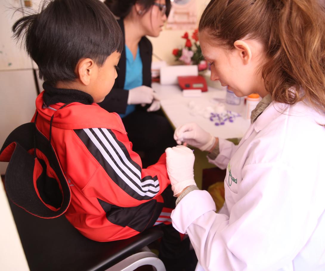 A young woman on a medical volunteer opportunity in South America checks blood sugar levels in Peru.