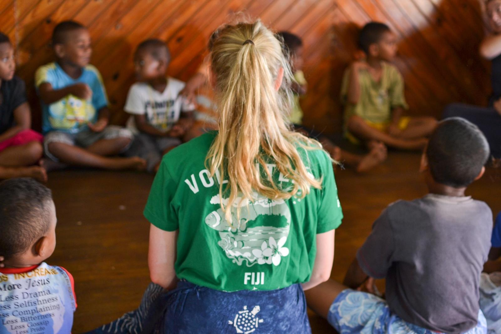 A Childcare volunteer working with children in Fiji sits in a circle with children during a kindergarten lesson.