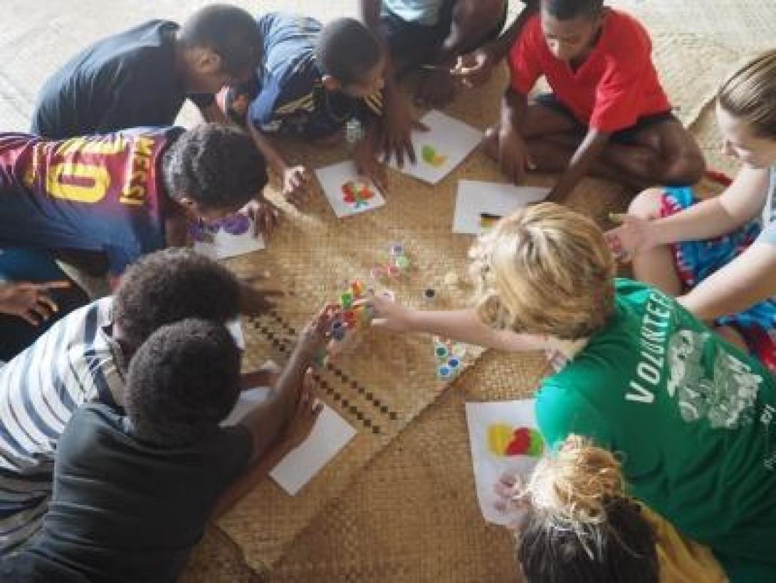 A Projects Abroad volunteer working with children in Fiji sits with a group of children at a special needs school teaching development skills through a painting activity.