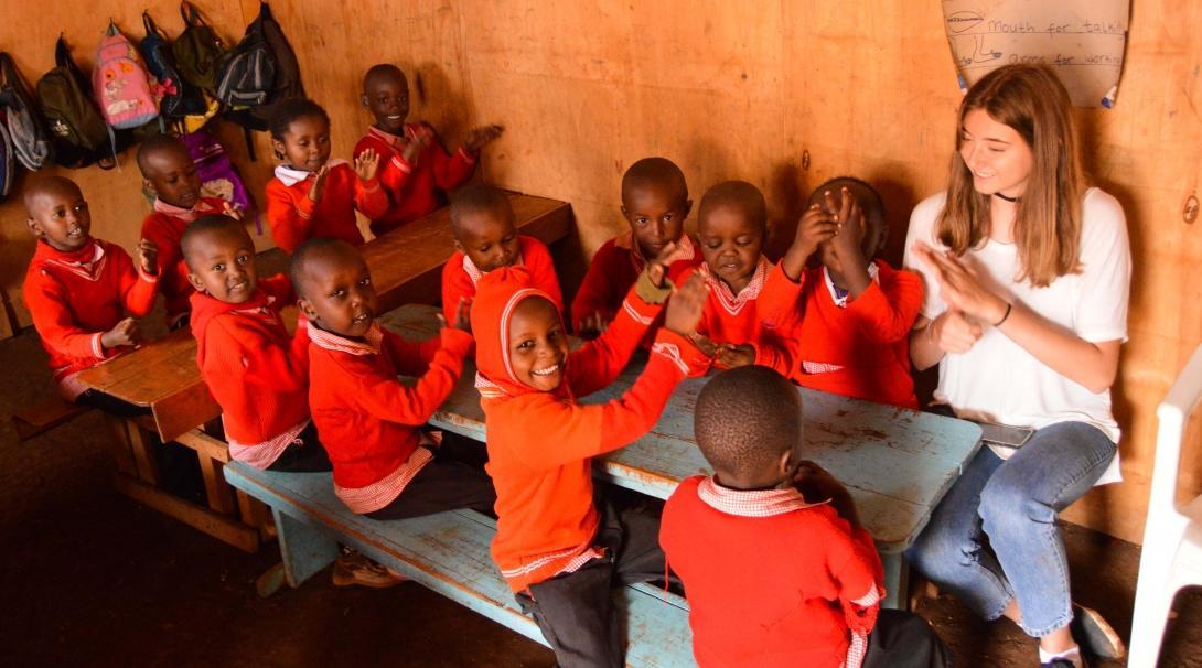 Female Projects Abroad volunteer working with children in Kenya sits with kindergarten children in a classroom during an educational activity.