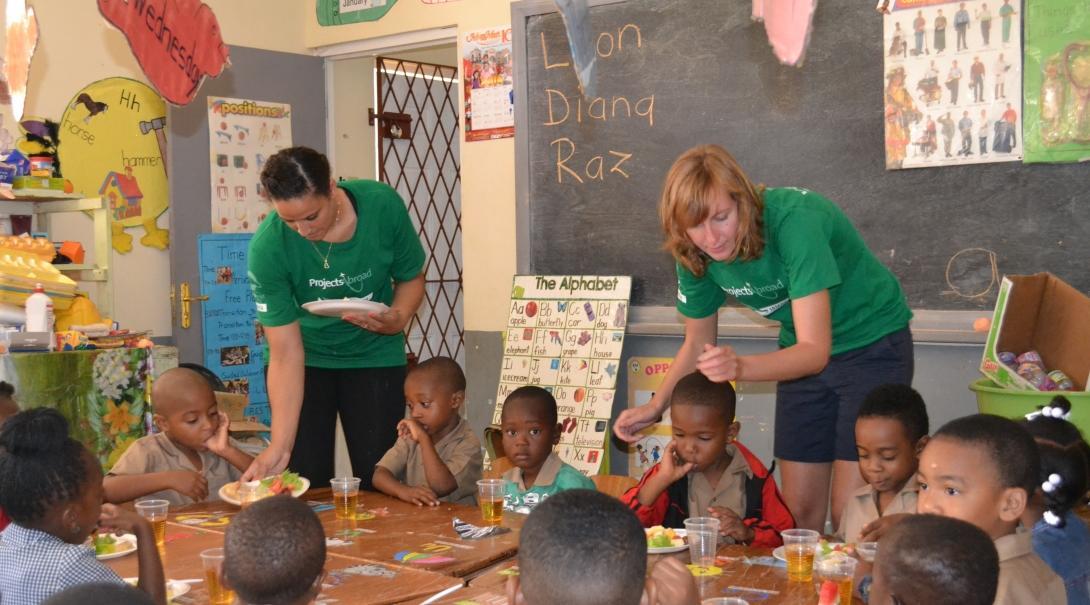 Two volunteers working with children in Jamaica serve breakfast to children at a kindergarten during a nutritional outreach.