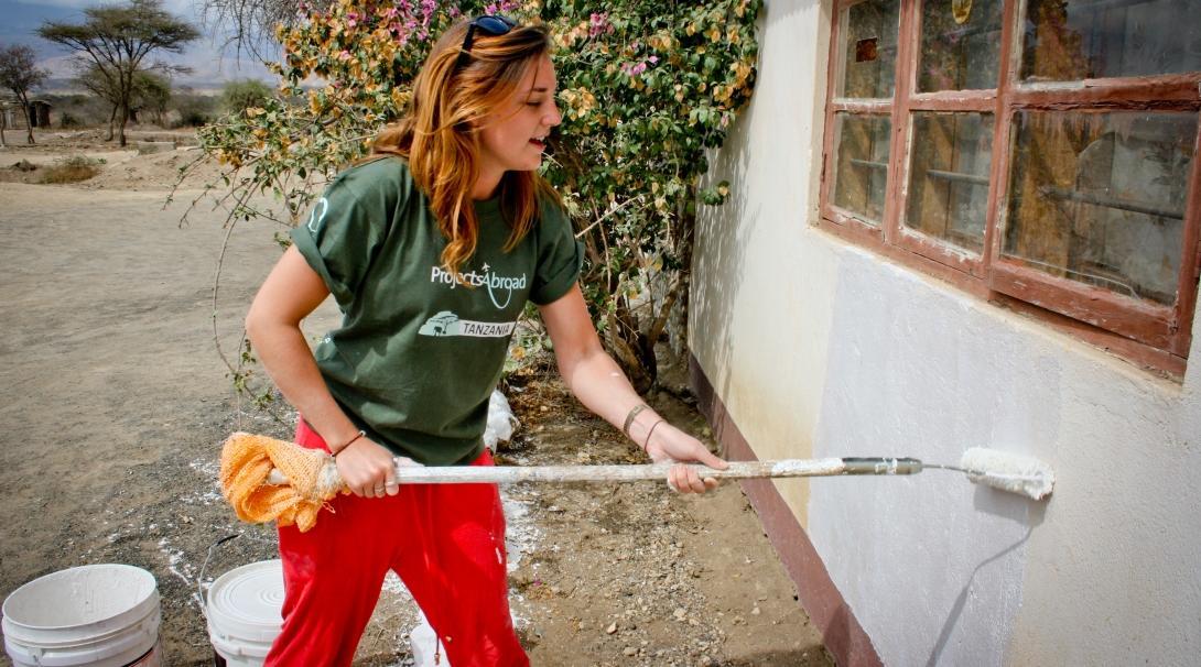 A female volunteer is seen painting a wall as part of her building volunteer work in Tanzania