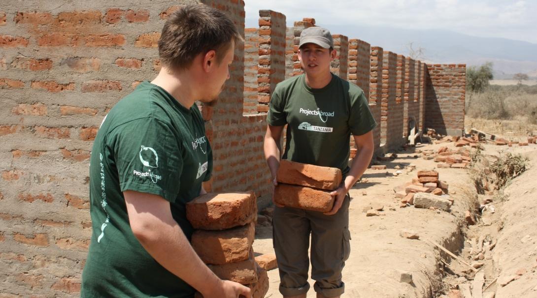 Two volunteers are seen carying bricks whilst on their building volunteer work in Tanzania with Projects Abroad