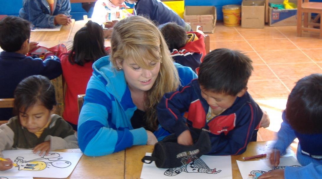 Projects Abroad Childcare volunteer helps children in Peru draw within a care centre placement.
