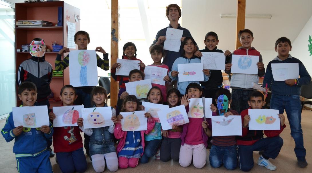 Projects Abroad male volunteer with children holding their drawings at a Childcare placement in Romania.