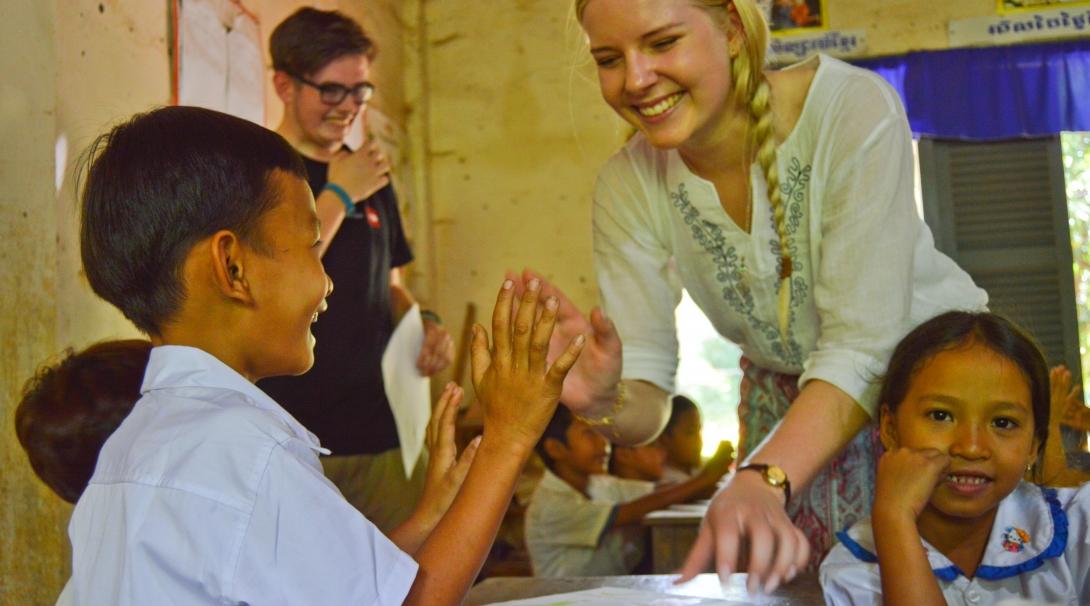 A young child gets a high five from a Projects Abroad volunteer working with children in Cambodia at a local kindergarten.