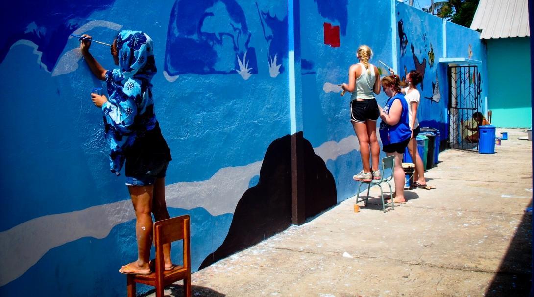 Female volunteers working with children in Ecuador paint a wall blue to help improve the learning environment at a kindergarten. 