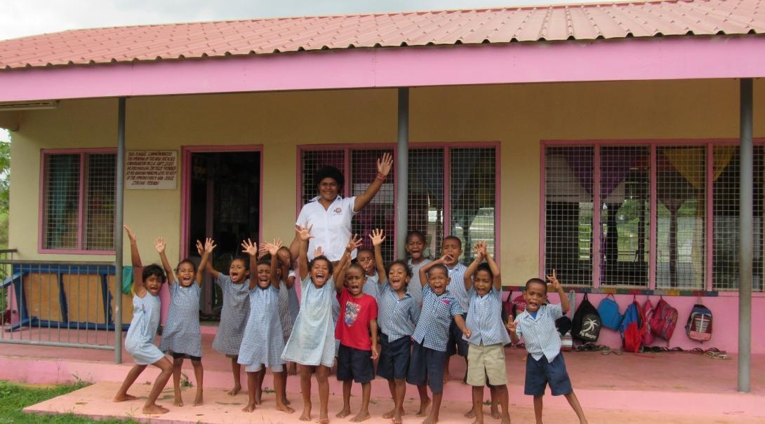 A group of children pose for a photo with their teacher outside a kindergarten at one of our Childcare volunteer placements in Fiji.