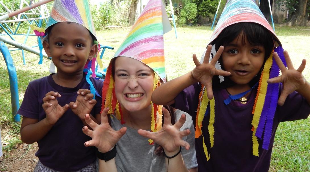 Female Childcare volunteer and children wear hats they have made during a fun activity on a Care placement in Sri Lanka.