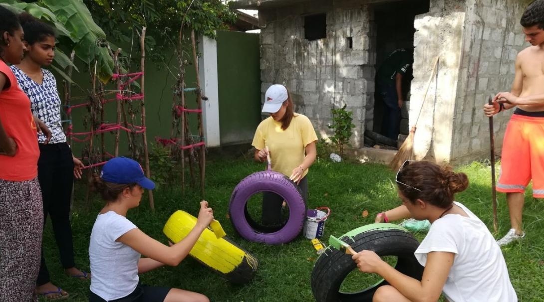 Childcare volunteers in Sri Lanka paint tyres for a multi-sensory garden at their Childcare placement.