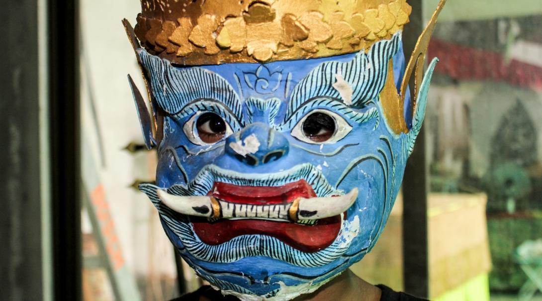 A volunteer over 50 learning about the Khmer culture in Cambodia, wears a traditional mask.
