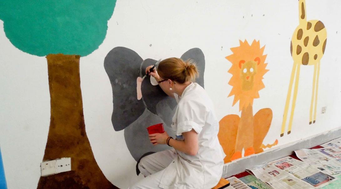 A volunteer over 50 doing childcare volunteering in Nepal, paints an educational mural on a wall. 