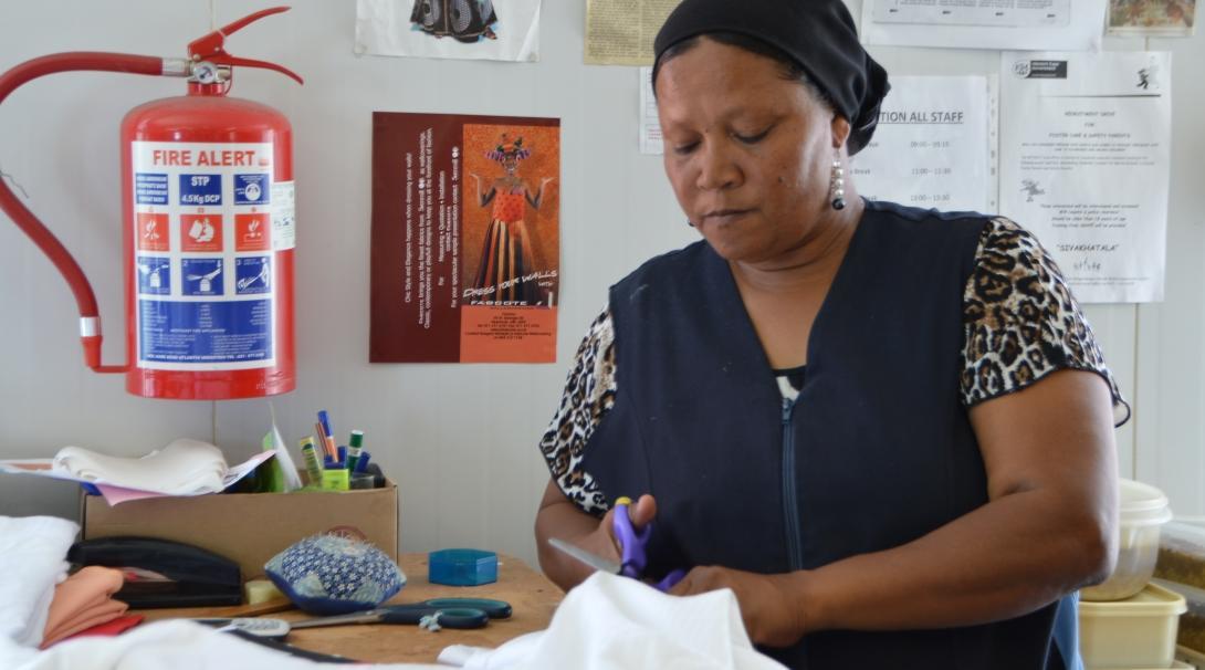 Female International Development Intern cuts with scissors through material during her work placement in South Africa.