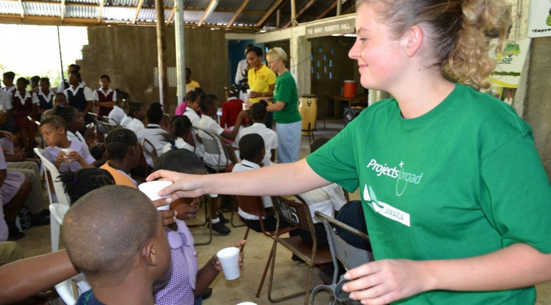 Psychology work experience in Jamaica shows Projects Abroad Childcare volunteer handing out hot drinks to school children during a HIV/Aids awareness presentation.