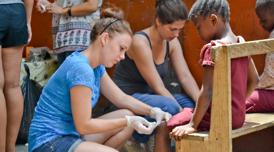 Female Medical worker bandages a young girls knee at a Medical Outreach Programme in Ghana.