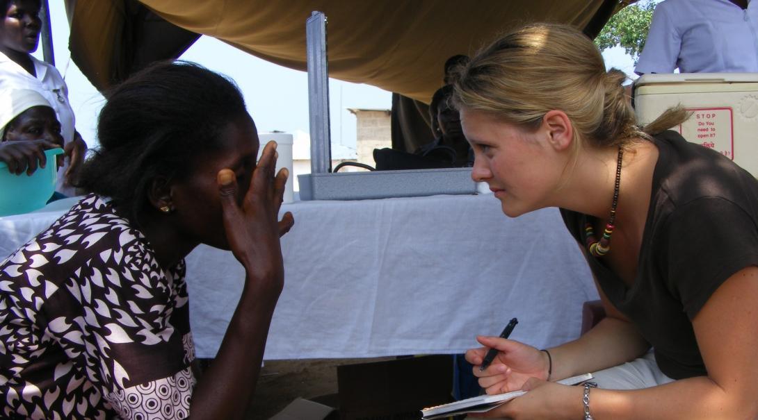 Female medical intern sits across a woman with a pad during Community Outreach programme in Ghana.