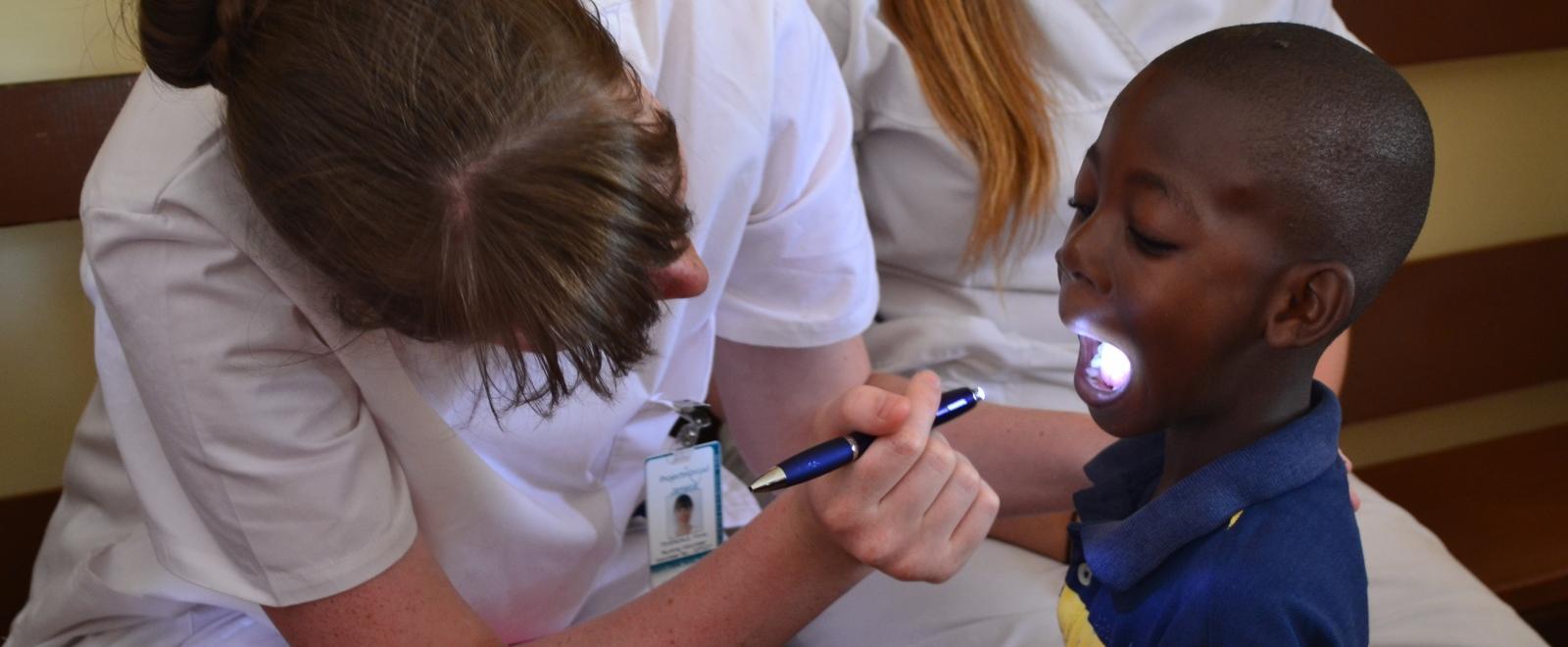 Female medical intern examines a young boy's mouth in a care centre during a medical internship in Jamaica.