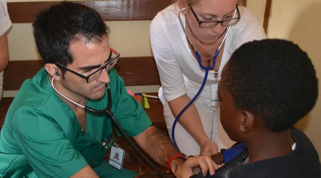 Male and female interns examine a young boy's chest at a Community Outreach Day in Jamaica.