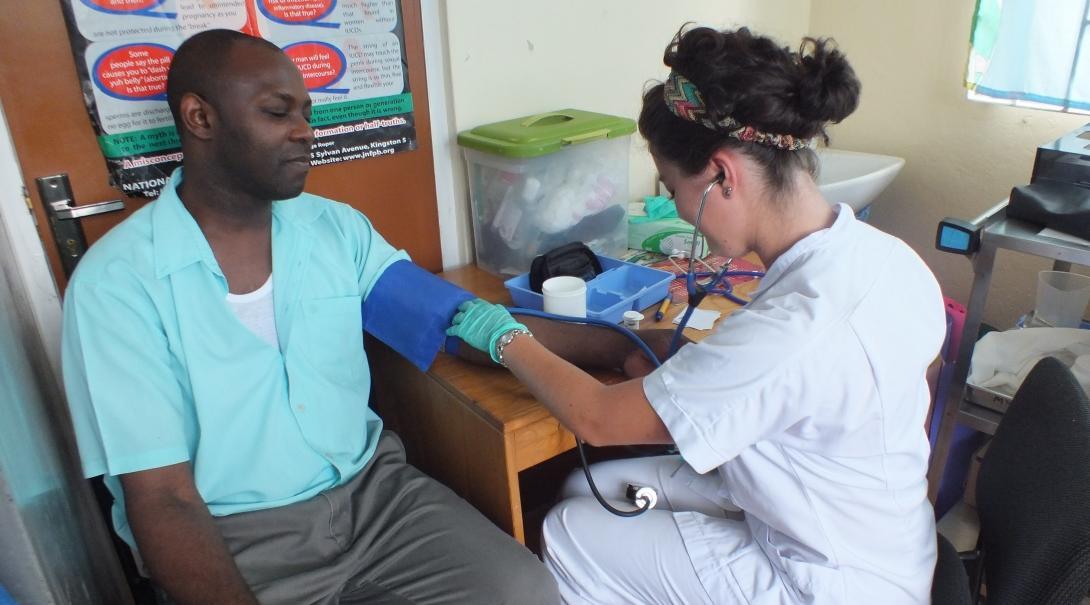 Female medical intern takes a local man's blood pressure in a Health Centre during a medical outreach in Jamaica.