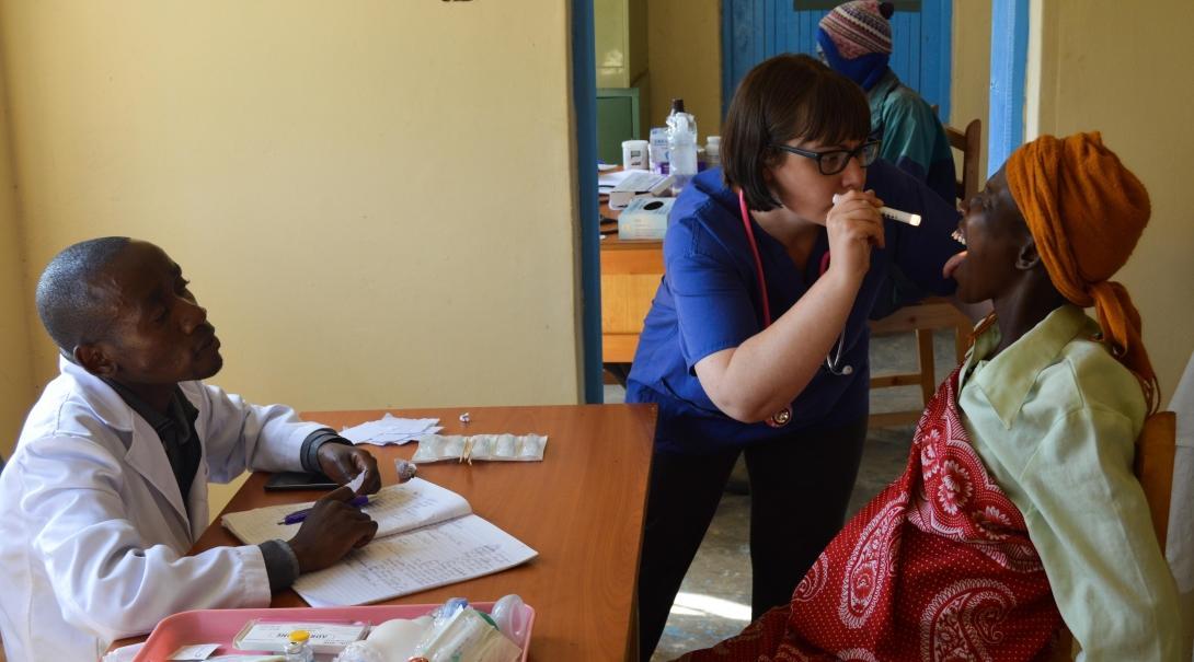 Female medical intern examines a woman's mouth with a healthcare worker at a medical outreach in Kenya.