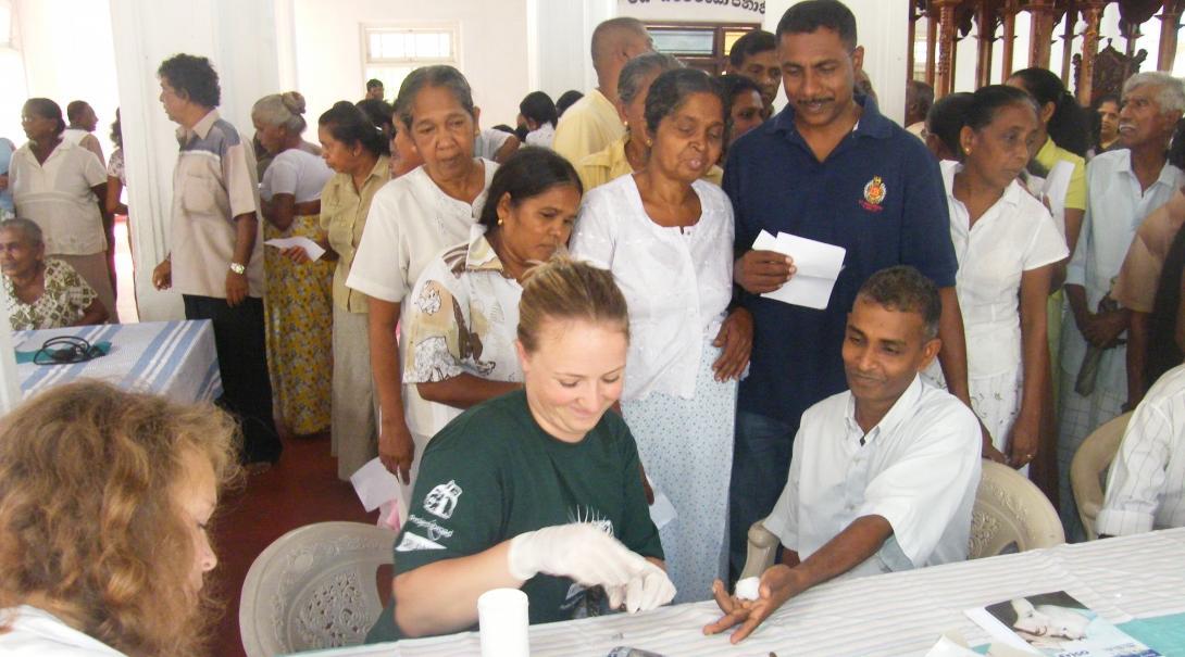 Two female interns on a nursing internship in Sri Lanka are seen helping at a medical camp assisting patients.