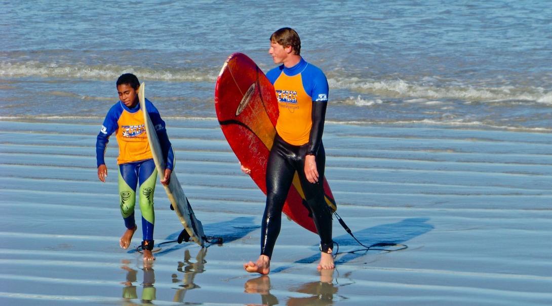 A young surfer and a volunteer walk along the beach during a project dedicated to teaching sport abroad.