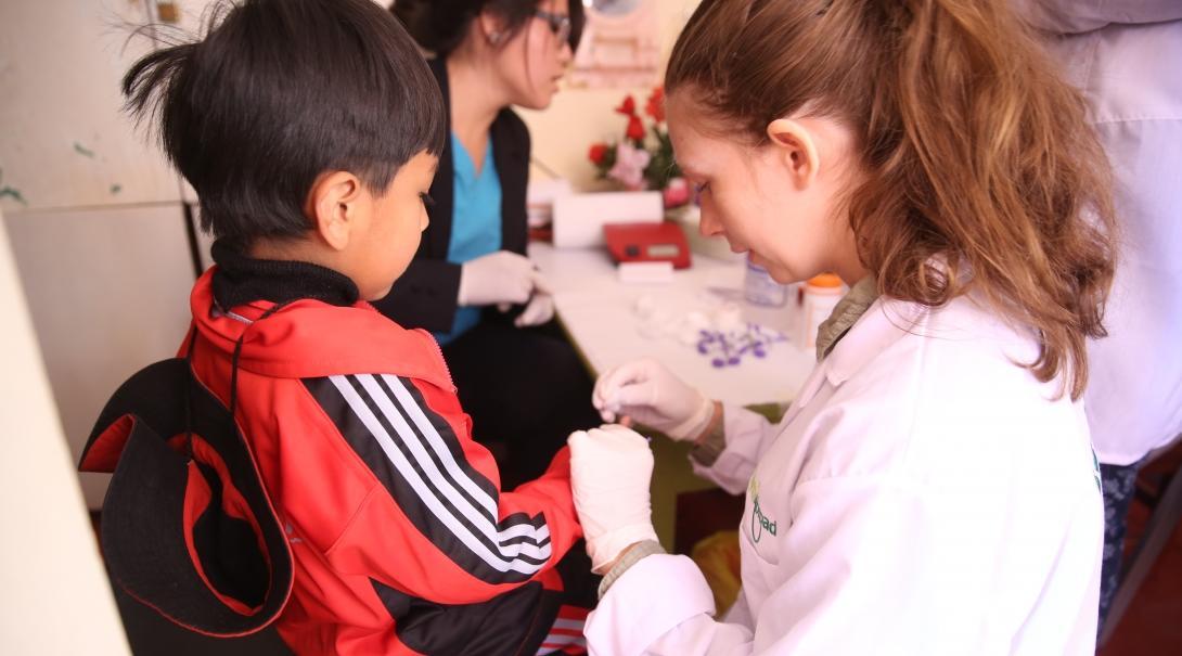 A female intern from Projects Abroad is seen drawing blood from a childs finger as part of her nursing internship in Peru.