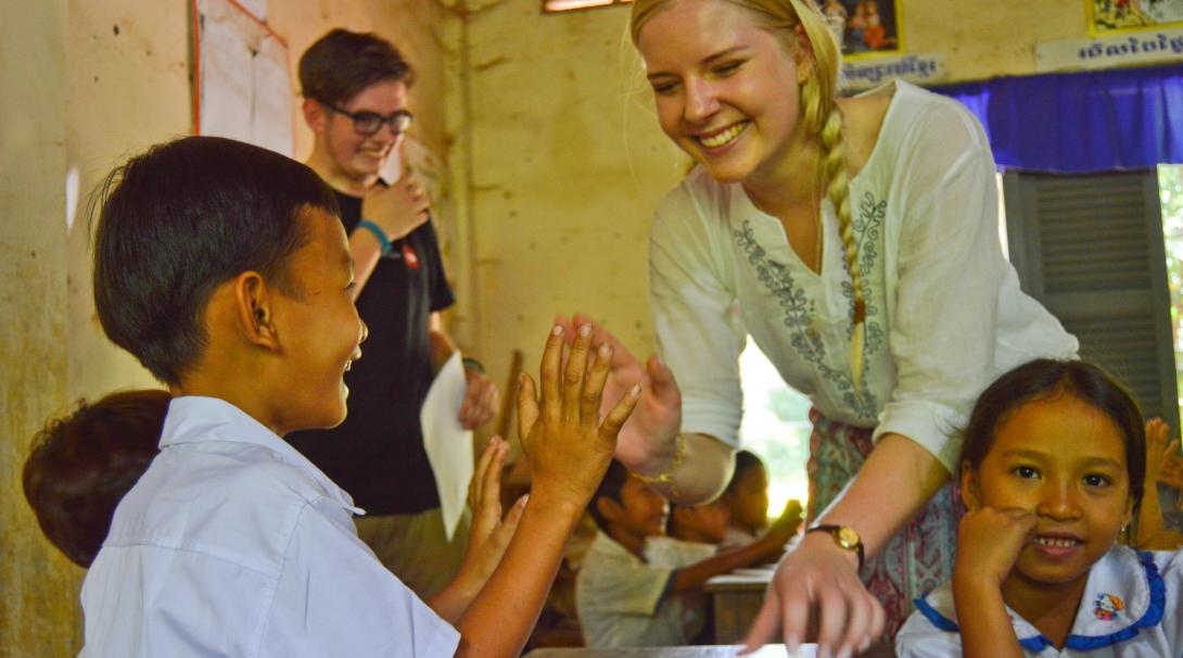 A teenage volunteer working with children in Cambodia gives a young child a high-five in the classroom. 