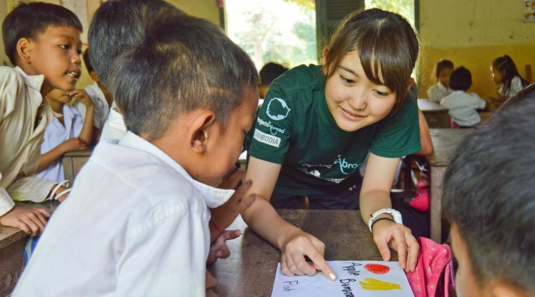 A teenage volunteer working with children in Cambodia helps a child with his English animal and fruit sight words. 
