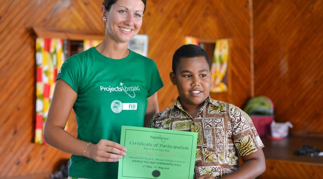A young boy hands over a certificate to a Projects Abrpad volunteer for her volunteer work with children for teenagers in Fiji