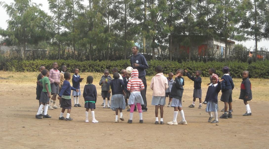 Volunteers and students stand in a circle while playing a game at the volunteer teaching placement in Kenya