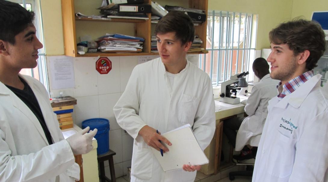 Male Dentistry interns are in white lab coats discussing a patient's file during their dentistry work experience in Tanzania.