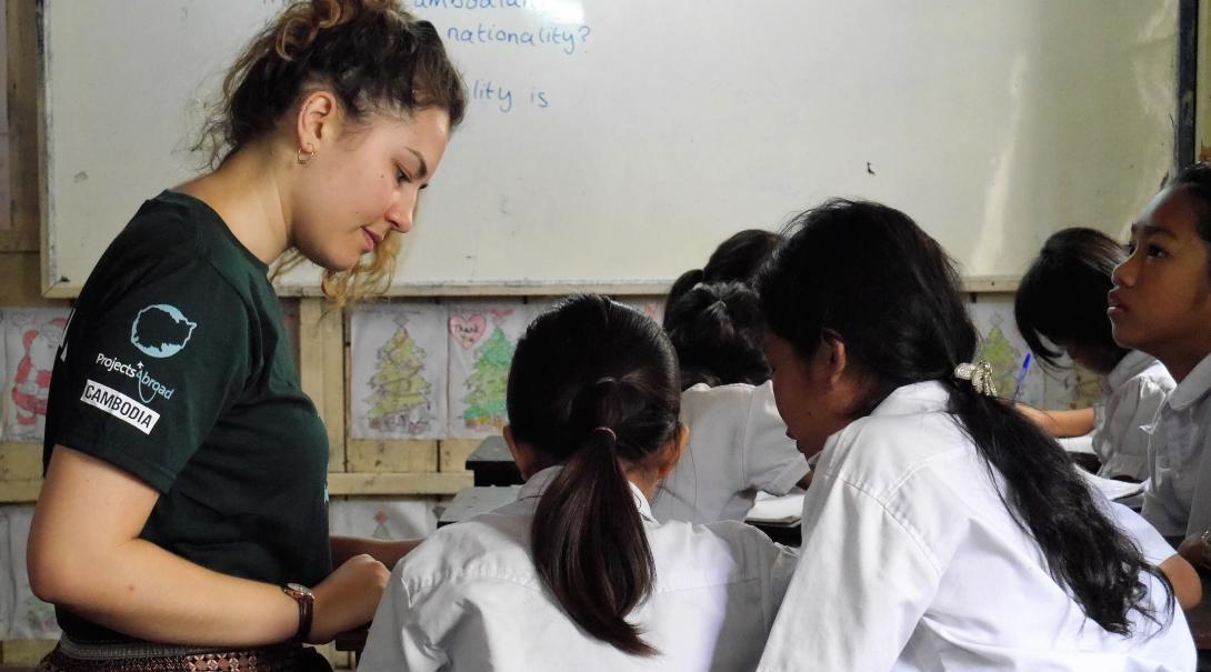 Two students receive class work assistance from a volunteer teaching English in Cambodia
