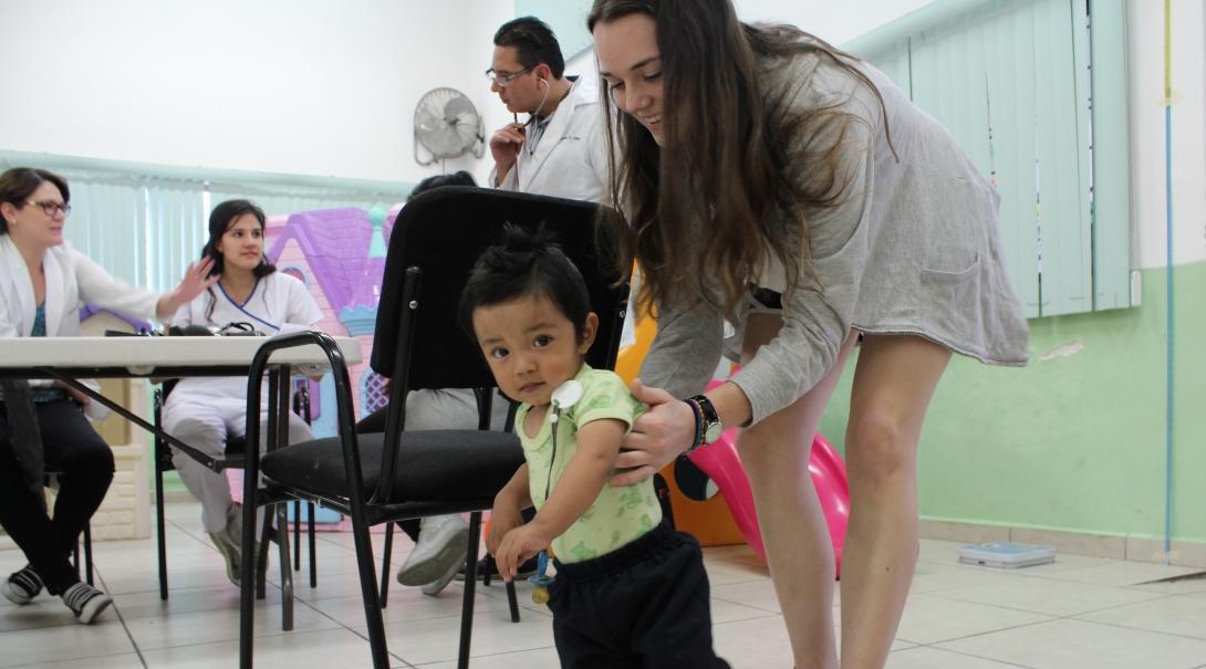 A female intern with Projects Abroad is pictured helping a child learn to walk as part of her physiotherapy internship in Mexico.
