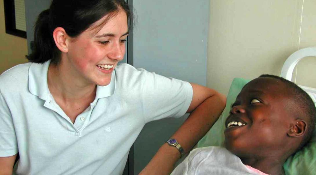 Projects Abroad female intern sat by the bedside of a young boy making him laugh during her physiotherapy internship in Ghana.