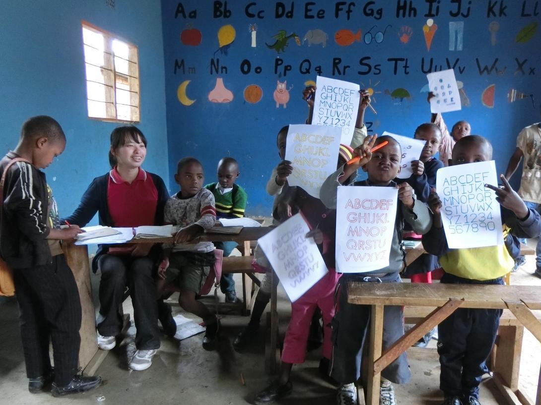 Children hold up their alphabet sheets to share with the volunteer teaching in Tanzania