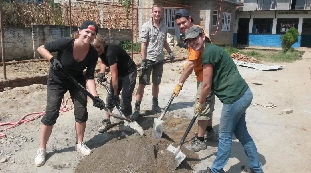 High school student volunteers doing building work in Nepal dig up sand needed for building work.
