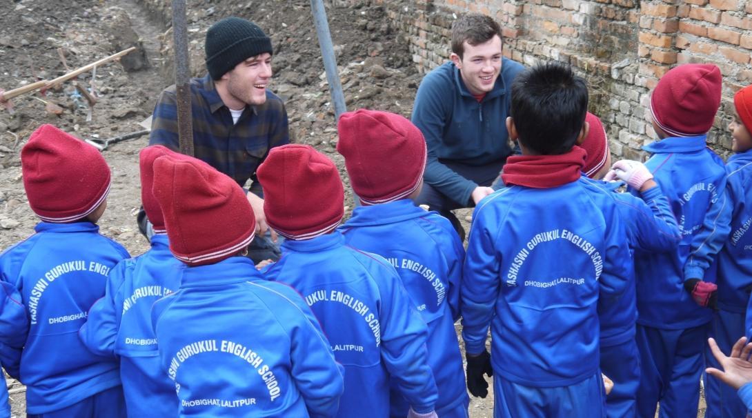 High school student volunteers doing building work in Nepal stop working to talk with young children.