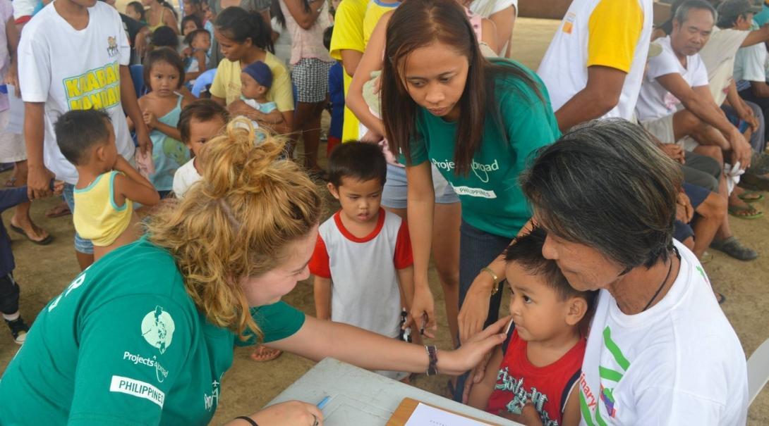 An intern from Projects Abroad is seen talking a to a young boy and his mother during her public health internship in the Phillippines.