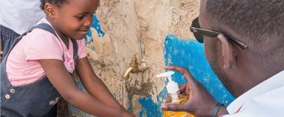 A Projects Abroad volunteer working with children in Kenya gives soap to a child washing their hands outdoors. 
