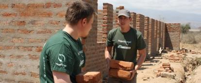 Teenage volunteers doing construction work in Tanzania carry bricks needed for a wall. 