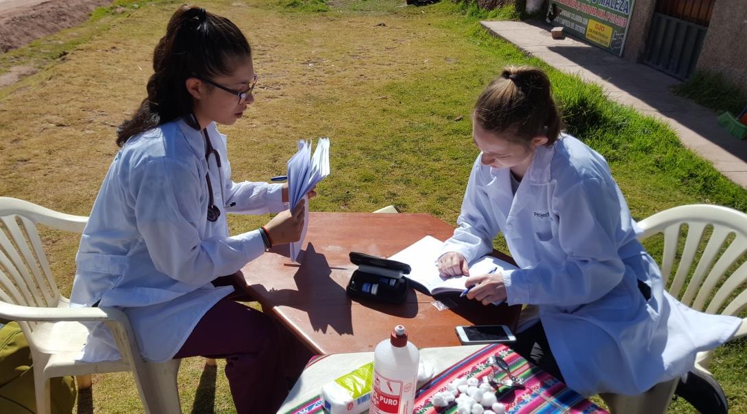 A pair of students completing Nursing internships abroad work through patients' notes after a community outreach in Peru.