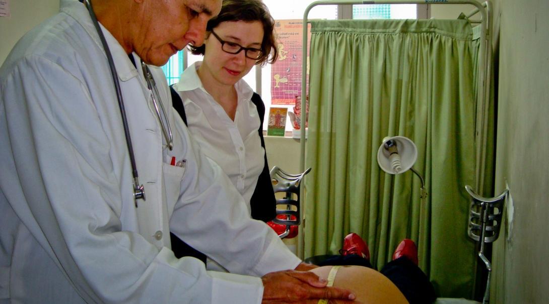 A local doctor treats a pregnant woman at a hospital while a student doing her Midwifery internship abroad watches.