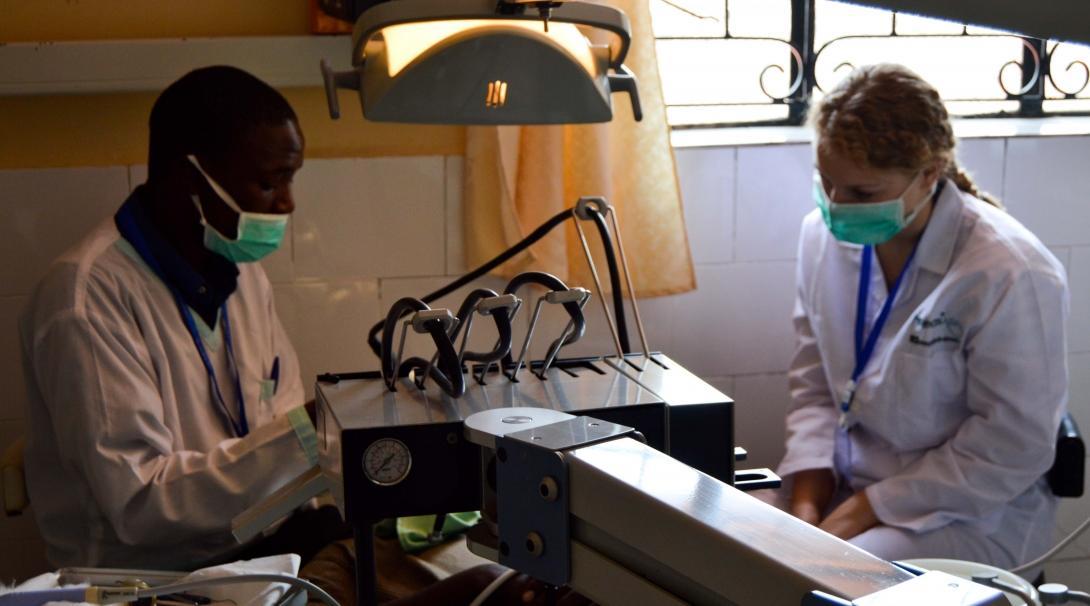 A dentist performs a dental procedure for a patient in Kenya as a student doing a Dentistry internship abroad observes.